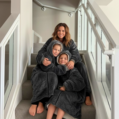 Woman and two children in matching dark gray blanky hoodies sitting on a staircase.