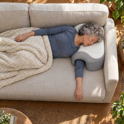Woman in her 60s napping on the sofa with her arm through the Cradle Pillow tunnel