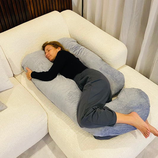 Woman sleeping on her side hugging the Cuddly Pillow™ U-shaped body pillow on a sofa