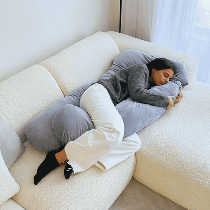 Woman sleeping on the grey Cuddly Pillow™ on a cream sofa