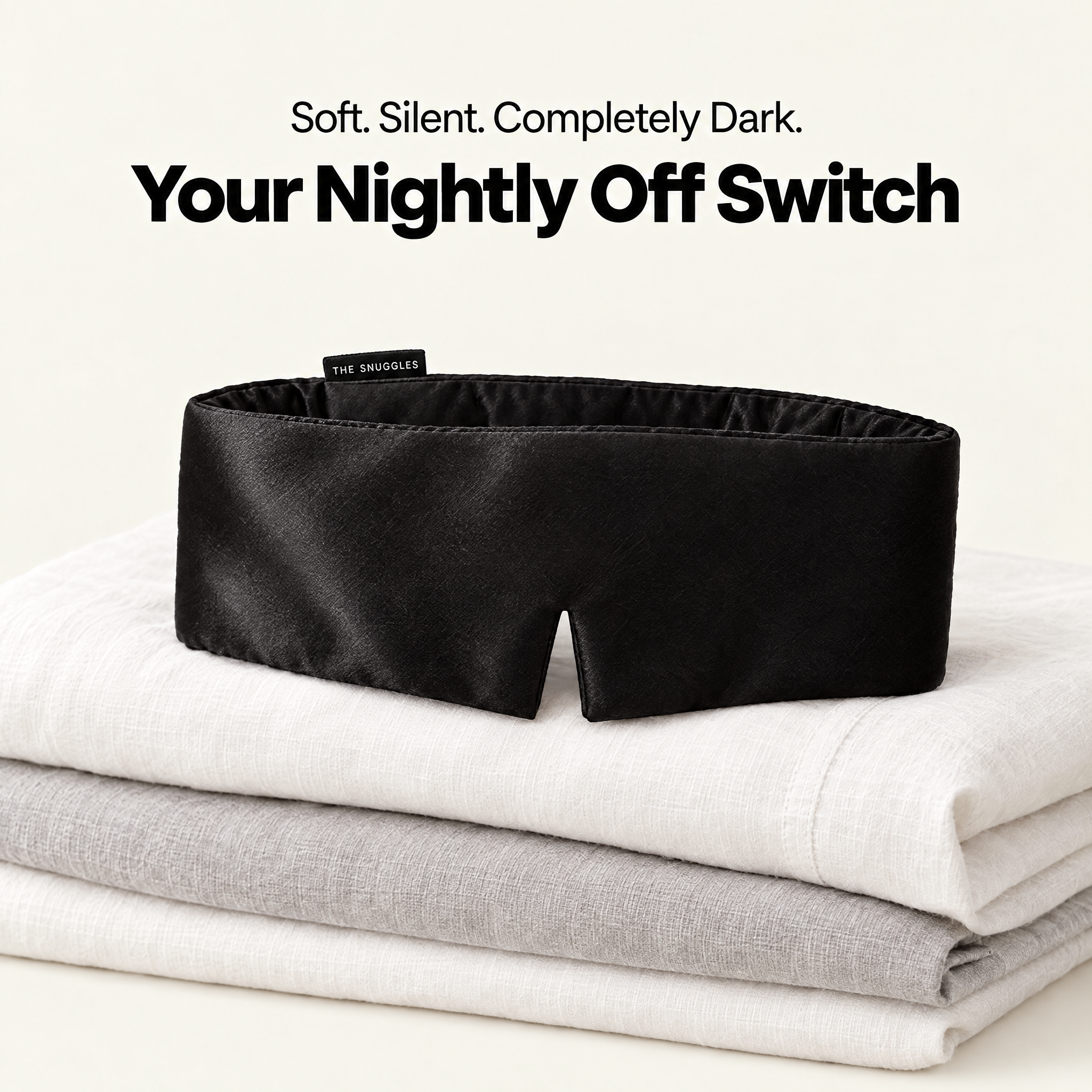 The Snuggles Silky Sleep Mask resting on folded linen bedding